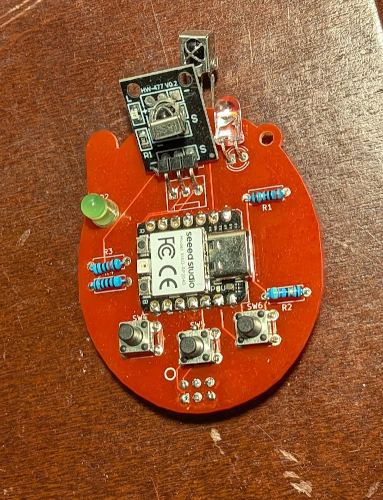 a PCB shaped like a tamagotchi with a seeed rp2350 zero in the middle, IR receiver and transmitter boards, and three buttons