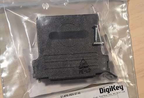 A black plastic molex D-Sub backshell in a plastic bag on top of another plastic bag with Digikey printed on it. The rest of the label is not visible.