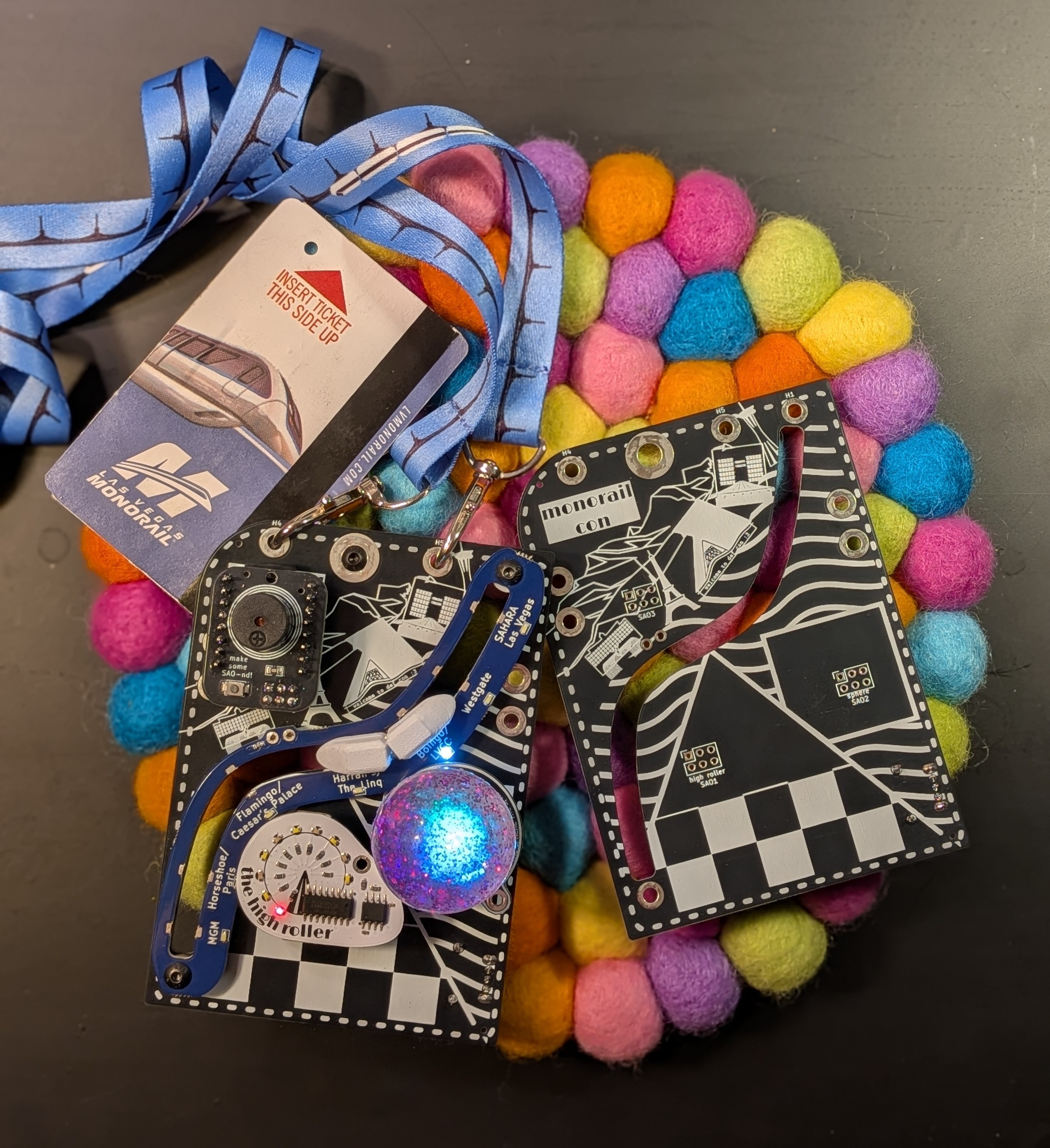 two badges, one with the SAOs attached and turned on. They are on a background of colorful wool 