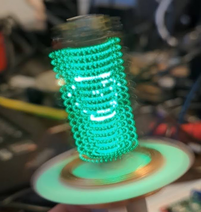 A raspberry pi pico with green LEDS strapped to it spinning really fast. You can kind of see a wireframe cube if you squint